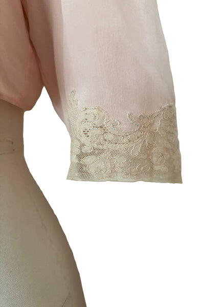 Detail view of 1930s vintage blush pink silk cream lace trimmed peter pan collared bed jacket, size extra small to small. Showing the elbow length lace trimmed sleeves.