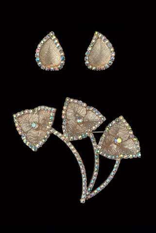 Vertical front view of 1960s vintage iridescent rhinestone and gold tone floral brooch and clip on earring jewelry set.