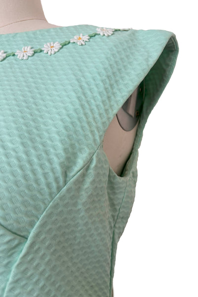 Detail view of 1960s vintage mint green cotton pique daisy trimmed sheath dress, size extra small to small. Showing minor discoloration under the arm.