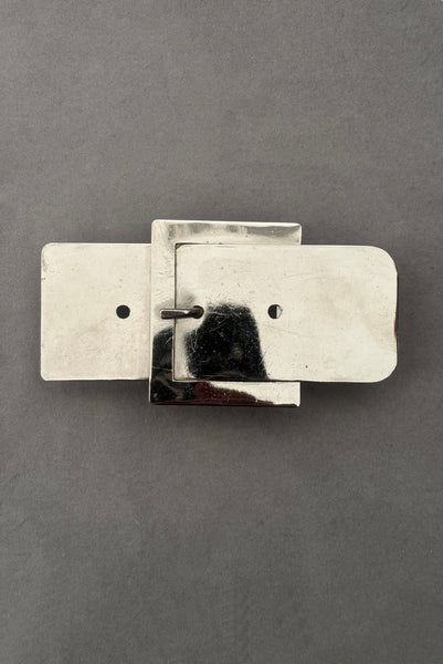 Vertical front view of 1980s vintage surrealist silver tone chrome belt buckle shaped novelty buckle.