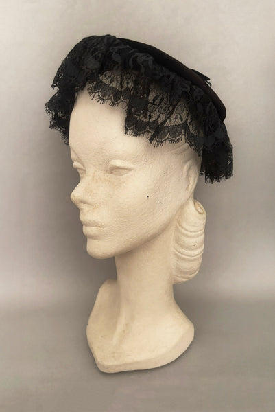 Vertical 3/4 view of 1950s vintage black velvet and lace one size pancake cocktail hat with ribbon and gold tone metal buckle, by Lemington for Frederick & Nelson.