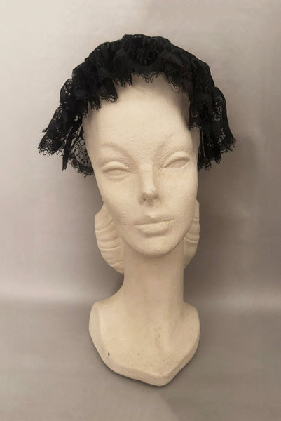 Vertical front view of 1950s vintage black velvet and lace one size pancake cocktail hat with ribbon and gold tone metal buckle, by Lemington for Frederick & Nelson.