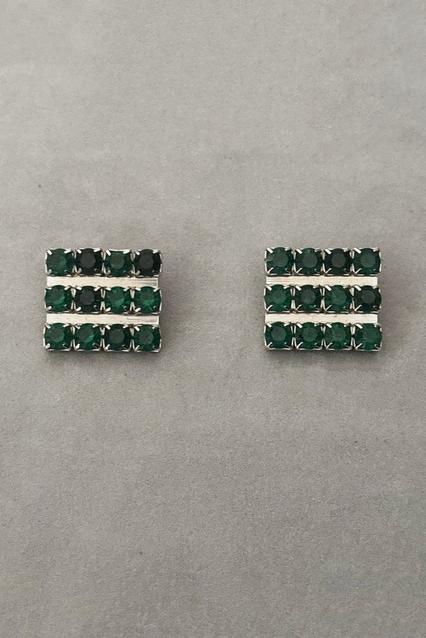 Vertical front view of 1960s vintage large rectangular silver tone and round emerald green rhinestone clip-on earrings.