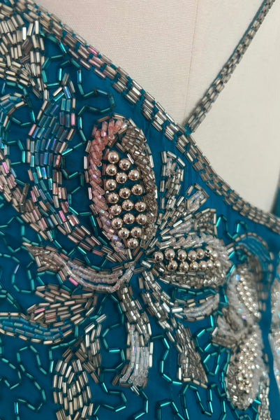 Detail view of 1980s vintage sweetheart neckline turquoise blue asymmetrical fringed beaded cocktail dress, size small to medium. Showing a small area of pink beading.
