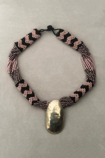 Vertical front view of 1970s vintage black and pale purple seed bead beadwork necklace with silver hammered oval pendant.