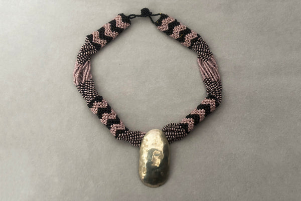 Horizontal front view of 1970s vintage black and pale purple seed bead beadwork necklace with silver hammered oval pendant.