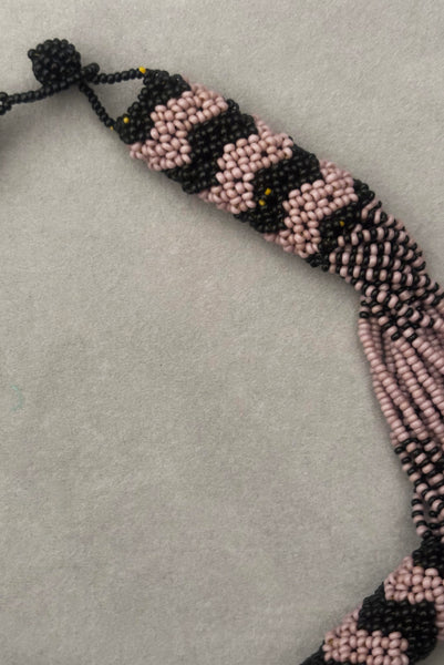 Detail view of 1970s vintage black and pale purple seed bead beadwork necklace with silver hammered oval pendant. Showing a close-up of the zig-zag beadwork.