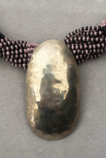 Detail view of 1970s vintage black and pale purple seed bead beadwork necklace with silver hammered oval pendant. Showing a close-up of the hammered silver oval pendant.