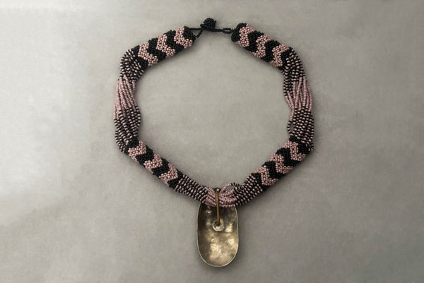 Horizontal back view of 1970s vintage black and pale purple seed bead beadwork necklace with silver hammered oval pendant.