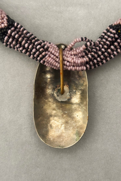 Detail view of 1970s vintage black and pale purple seed bead beadwork necklace with silver hammered oval pendant. Showing the back of the hammered silver oval pendant.