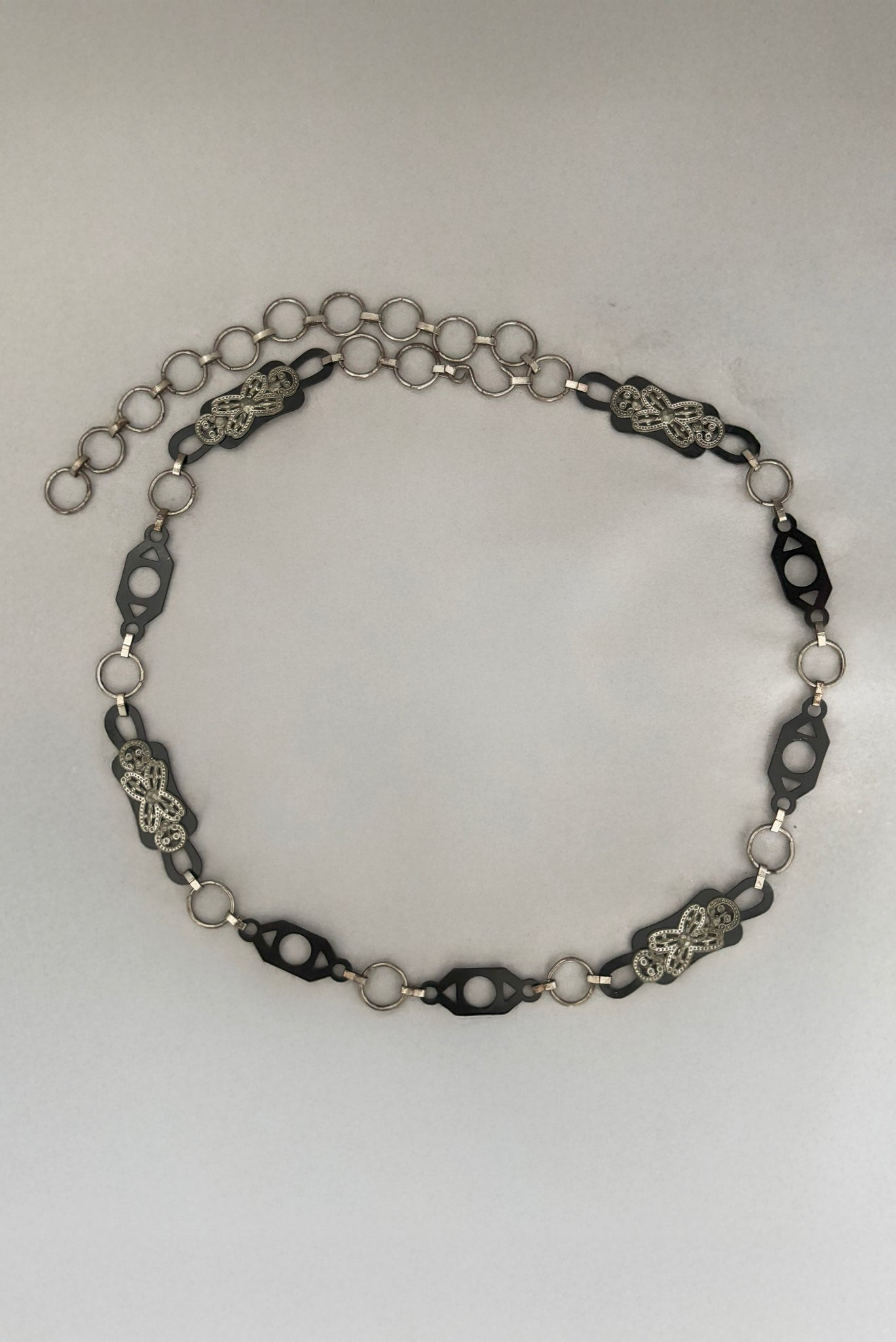 Vertical top view of 1930s vintage black celluloid and silver tone metal filigree link belt.