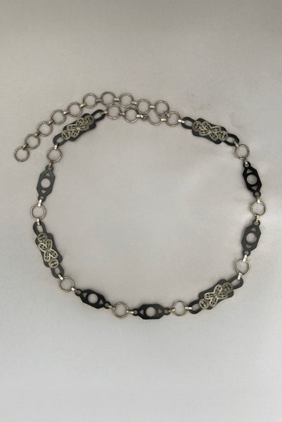 Vertical top view of 1930s vintage black celluloid and silver tone metal filigree link belt.