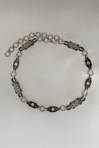 Vertical top view of 1930s vintage black celluloid and silver tone metal filigree link belt.