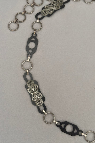 Detail view of 1930s vintage black celluloid and silver tone metal filigree link belt. Showing a close-up of the black celluloid and silver tone metal filigree links.