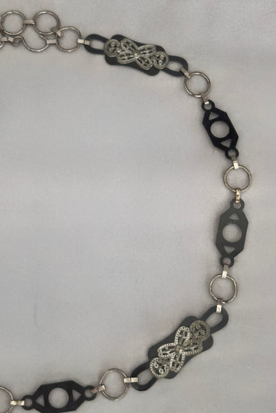 Detail view of 1930s vintage black celluloid and silver tone metal filigree link belt. Showing a close-up of the black celluloid and silver tone metal filigree links.