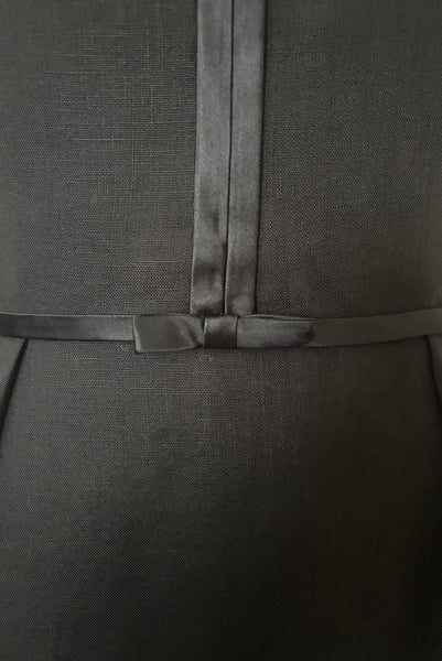 Detail view of 1950s vintage black imported linen satin and bow trimmed sheath dress, size small to medium. Showing the satin string belt and bow at the waistline.