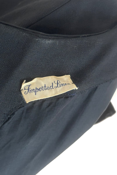 Interior detail view of 1950s vintage black imported linen satin and bow trimmed sheath dress, size small to medium. Showing the linen facing, synthetic lining, and imported linen label.