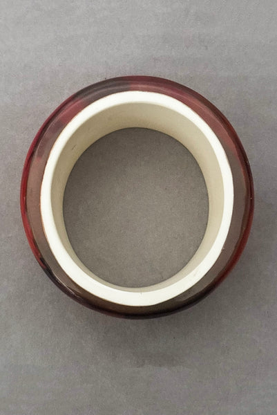 Vertical top view of 1960s vintage pink, mustard yellow, orange, and purple wide floral clear Lucite oval bangle bracelet with white interior.