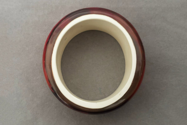 Horizontal top view of 1960s vintage pink, mustard yellow, orange, and purple wide floral clear Lucite oval bangle bracelet with white interior.