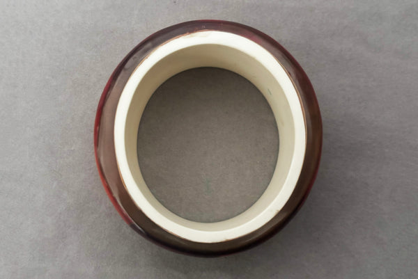Horizontal bottom view of 1960s vintage pink, mustard yellow, orange, and purple wide floral clear Lucite oval bangle bracelet with white interior.