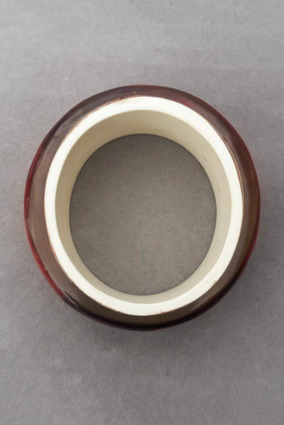 Vertical bottom view of 1960s vintage pink, mustard yellow, orange, and purple wide floral clear Lucite oval bangle bracelet with white interior.