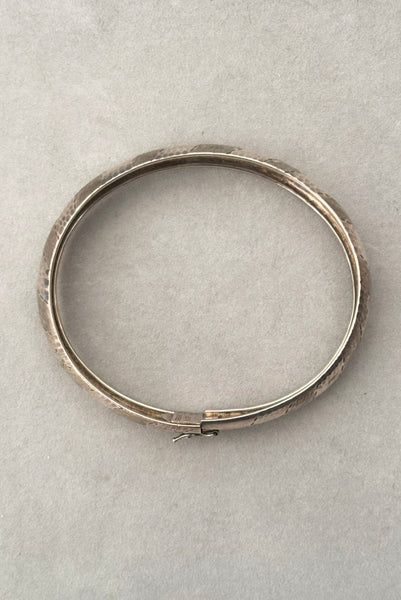 Vertical top view of 1970s vintage stripe engraved Italian 925 sterling silver bangle bracelet made in Salerno, Italy. Showing the slide clasp with hinged latch.