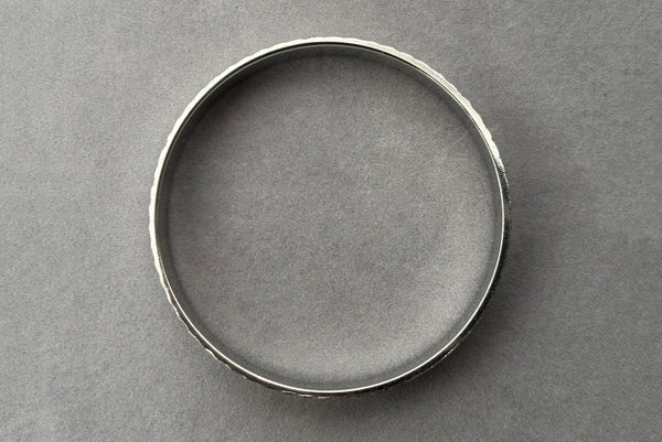 Horizontal top view of 1980s vintage petite silver tone chrome engraved bangle bracelet by Monet, size small.