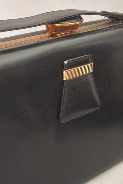 Detail view of 1930s vintage Art Deco black leather gold frame handbag by Evans with coin purse, mirror, comb, and lipstick holder. Showing wear to the edge of the leather detail on the front.