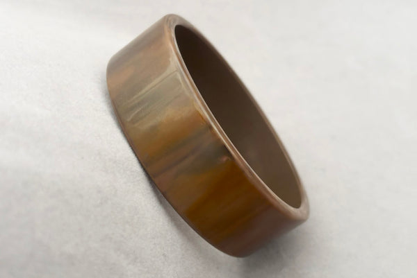 Horizontal perspective view of 1950s vintage gray and brown marbled Lucite plastic sliced bangle bracelet.