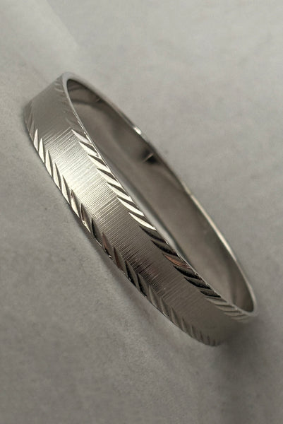 Vertical perspective view of 1980s vintage petite silver tone chrome engraved bangle bracelet by Monet, size small.