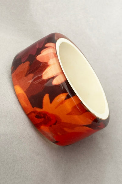 Vertical perspective view of 1960s vintage pink, mustard yellow, orange, and purple wide floral clear Lucite oval bangle bracelet with white interior.