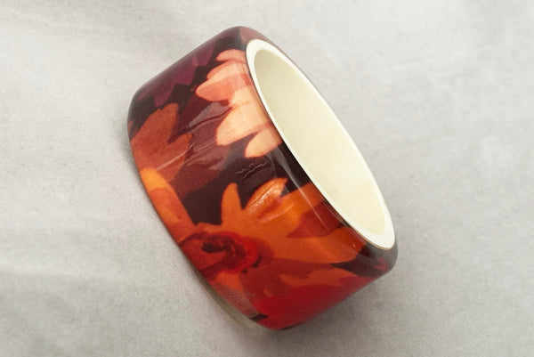 Horizontal perspective view of 1960s vintage pink, mustard yellow, orange, and purple wide floral clear Lucite oval bangle bracelet with white interior.