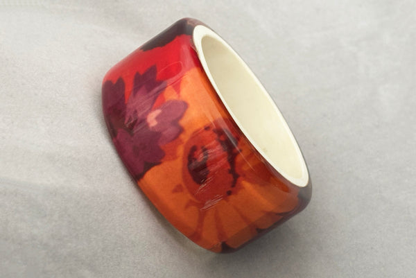 Horizontal perspective view of 1960s vintage pink, mustard yellow, orange, and purple wide floral clear Lucite oval bangle bracelet with white interior. Showing the scratched area.