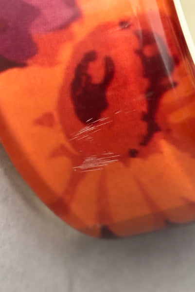 Detail view of 1960s vintage pink, mustard yellow, orange, and purple wide floral clear Lucite oval bangle bracelet with white interior. Showing a close-up of the scratched area.