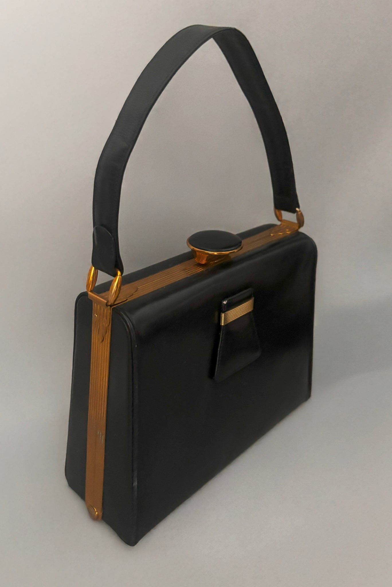 Vertical perspective view of 1930s vintage Art Deco black leather gold frame handbag by Evans with coin purse, mirror, comb, and lipstick holder.