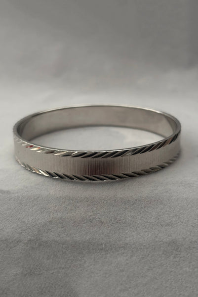 Vertical front view of 1980s vintage petite silver tone chrome engraved bangle bracelet by Monet, size small.
