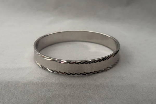 Horizontal front view of 1980s vintage petite silver tone chrome engraved bangle bracelet by Monet, size small.