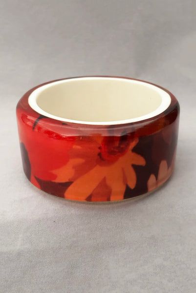 Vertical front view of 1960s vintage pink, mustard yellow, orange, and purple wide floral clear Lucite oval bangle bracelet with white interior.