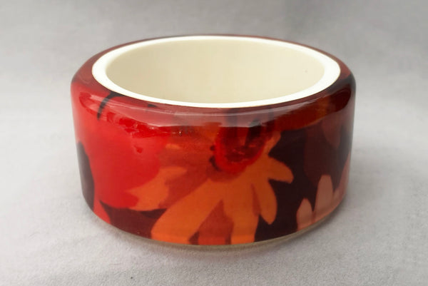 Horizontal front view of 1960s vintage pink, mustard yellow, orange, and purple wide floral clear Lucite oval bangle bracelet with white interior.
