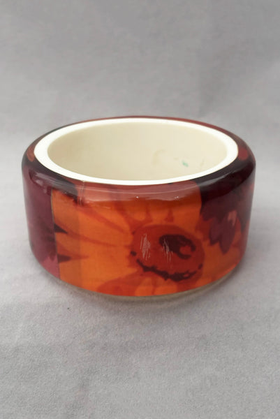 Vertical back view of 1960s vintage pink, mustard yellow, orange, and purple wide floral clear Lucite oval bangle bracelet with white interior. Showing the scratched area.