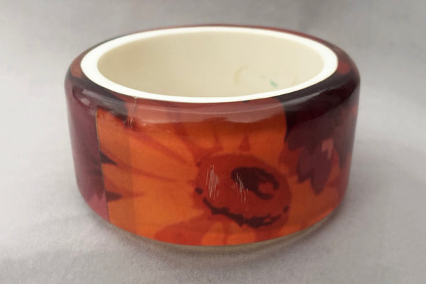 Horizontal back view of 1960s vintage pink, mustard yellow, orange, and purple wide floral clear Lucite oval bangle bracelet with white interior. Showing the scratched area.