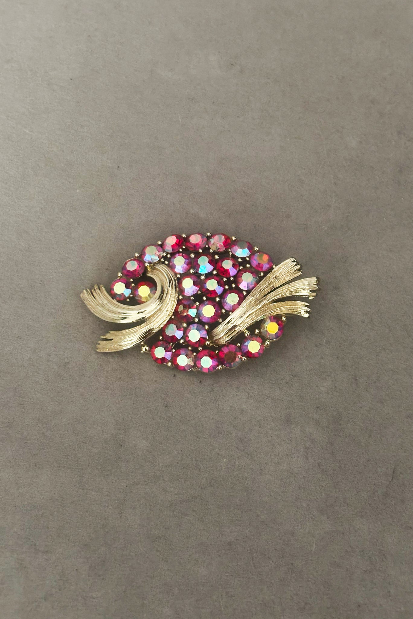 Vertical front view of 1950s vintage oval iridescent fuchsia pink rhinestone and champagne metal brooch, by Lisner.