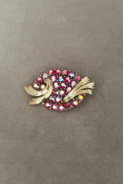 Vertical front view of 1950s vintage oval iridescent fuchsia pink rhinestone and champagne metal brooch, by Lisner.