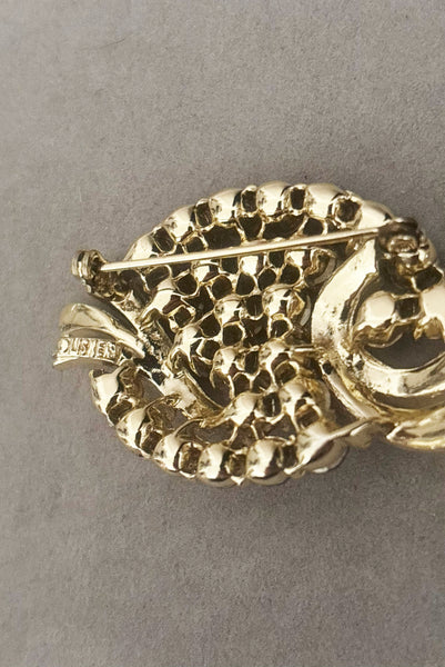 Detail view of 1950s vintage oval iridescent fuchsia pink rhinestone and champagne metal brooch, by Lisner. Showing the Lisner maker's mark.