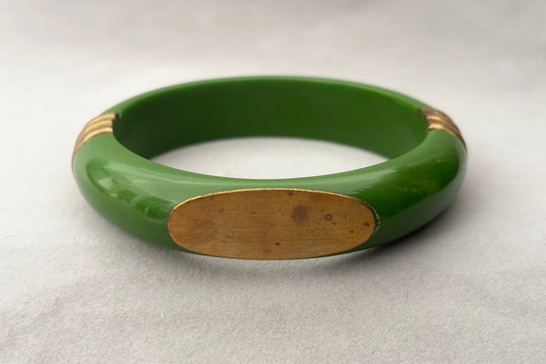 Horizontal front view of 1970s vintage green plastic and brass bangle bracelet, made in India. Showing some spots on the brass plate.
