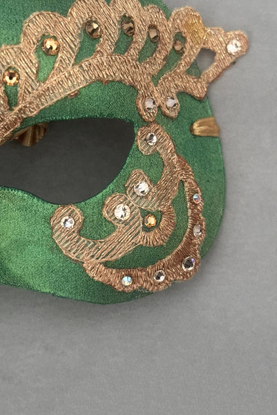 Vertical detail view of 1990s gold Lurex lace, gold Swarovski crystal, and metallic green painted half mask with gold satin ribbon ties. Showing the light gold and gold Swarovski crystals.