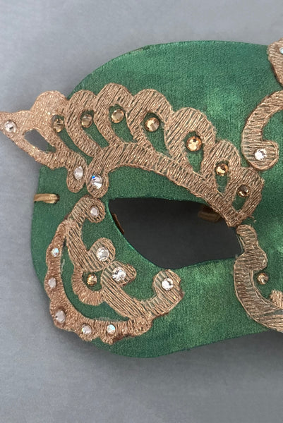 Vertical detail view of 1990s gold Lurex lace, gold Swarovski crystal, and metallic green painted half mask with gold satin ribbon ties. Showing the light gold and gold Swarovski crystals.