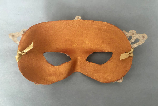 Horizontal back view of 1990s gold Lurex lace, gold Swarovski crystal, and metallic pink rose gold painted half mask with gold satin ribbon ties. Showing the inside of the mask.