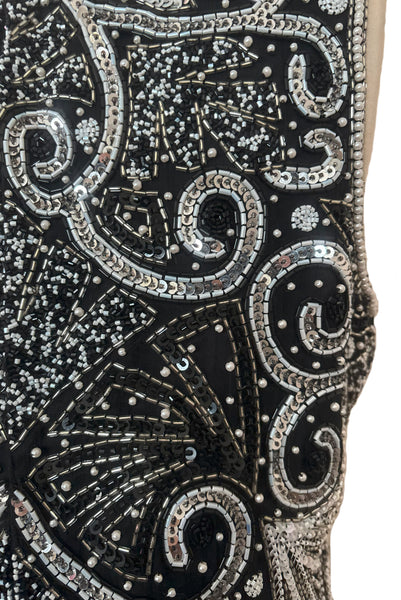 Detail view of 1980s vintage Art Deco faux pearl, silver and black glass beaded black silk chiffon evening dress, size small to medium. With a scoop neckline, sleeveless bodice, and floor length pencil skirt. Showing a close up of the bodice with the silver, white, and black bead and sequin embellished Deco style motif.