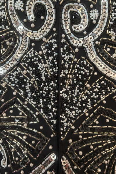 Detail view of 1980s vintage Art Deco faux pearl, silver and black glass beaded black silk chiffon evening dress, size small to medium. With a scoop neckline, sleeveless bodice, and floor length pencil skirt. Showing a close up of the bodice with the silver, white, and black bead and sequin embellished Deco style motif.